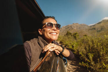 Porträt einer schönen jungen Frau mit Sonnenbrille, die an einem sonnigen Tag durch das Autofenster nach draußen schaut. Asiatische Frau auf einer Autoreise. - JLPSF26273