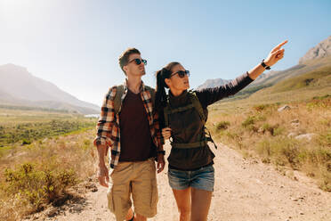 Junger Mann und Frau wandern auf einem Wanderweg. Junges Paar mit Rucksack wandern auf einem extremen Gelände, mit Frau zeigt weg. - JLPSF26276