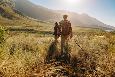 Rückansicht eines jungen Mannes und einer Frau, die auf einem Wanderweg durch die Landschaft wandern. Junges Paar mit Rucksack beim Wandern in extremem Gelände. - JLPSF26279