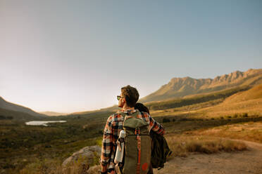 Couple of hikers enjoying view. Young couple hiking in nature. Rear view of  man and woman with backpacks standing together on country road. stock photo