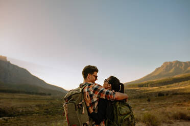 Rear view shot of young couple standing together in countryside and looking at each other. Tourist hiking in nature. - JLPSF26293