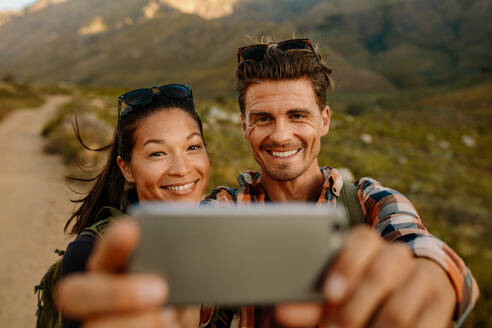 Junger Mann und Frau machen ein Selfie auf einer Wanderung auf dem Land. Junges Paar wandert im Naturschutzgebiet und macht Fotos mit dem Smartphone. - JLPSF26295