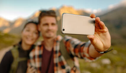 Wandererpaar macht Selfie mit Smartphone. Junger Mann und Frau machen Selbstporträt auf einer Wanderung. Fokus auf Handy. - JLPSF26296