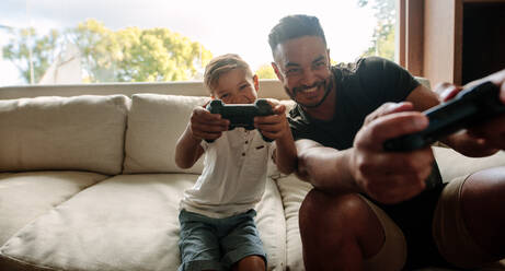 Portrait of father and son enjoying playing video game in living room. Smiling young man and little boy playing video game at home. - JLPSF26305