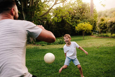 Vater und Sohn spielen Fußball im Garten. Glücklicher kleiner Junge spielt Fußball mit seinem Vater. - JLPSF26310