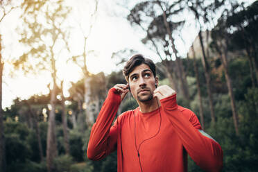 Man wearing earphones looking away. Runner listening to music during morning jog. - JLPSF26312