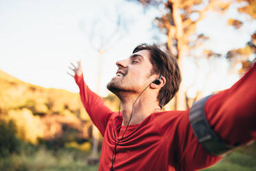 Ein Mann genießt die Natur und hört Musik in einem Park. Ein Läufer entspannt sich mit geschlossenen Augen nach dem Training. - JLPSF26315