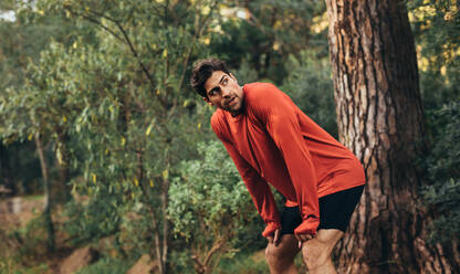 Man relaxing after intense workout. Athlete taking rest with hands resting on knees after a run. - JLPSF26317