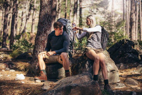 Ein Mann und eine Frau entspannen sich beim Trekking im Wald. Ein Wandererpaar macht eine Pause, sitzt auf einem Felsen und trinkt Wasser. - JLPSF26327