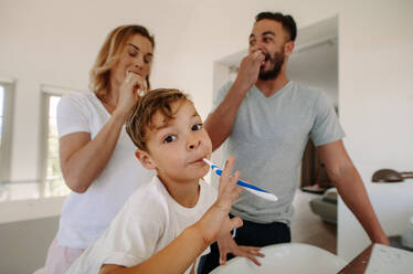 Little boy brushing teeth with his parents in bathroom. Family brushing teeth together in bathroom. - JLPSF26348