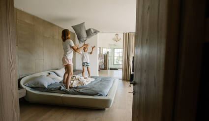 Mother and son standing on bed and playing with pillows. Young woman and little boy playing with pillows in bedroom. - JLPSF26360