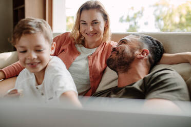 Smiling young woman relaxing on sofa with her husband and son. Happy young family relaxing on couch at home. - JLPSF26362