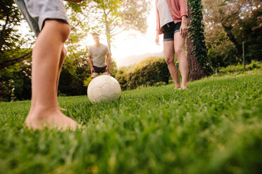 Football on grass with family standing around outdoors in park. Legs of little boy about to play football with his parents in garden. - JLPSF26366