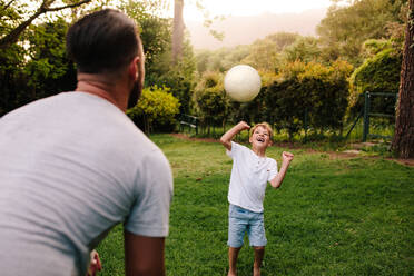 Vater und Sohn spielen mit einem Fußball im Hinterhofgarten. Glücklicher kleiner Junge, der seinem Vater den Ball zuspielt. - JLPSF26368