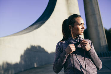 Healthy young woman in sportswear standing outdoors in morning and looking away. - JLPSF26372