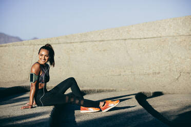 Healthy woman sitting on steps after exercise session. Female fitness model relaxing outdoors. - JLPSF26377