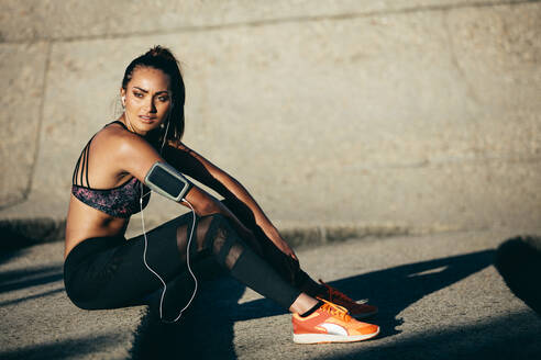 Schlanke und fitte Frau, die nach dem morgendlichen Training im Freien sitzt. Weibliches Fitnessmodell, das auf Stufen sitzt. - JLPSF26378