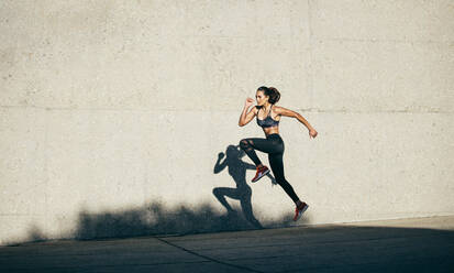 Dedicated female athlete exercising on sidewalk against white wall stock  photo