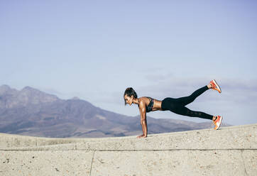 Muscular young woman doing push ups. Side view shot of healthy young female doing core workout outdoors. - JLPSF26396