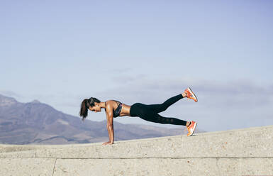 Young muscular woman doing core exercise outdoors. Fit female doing press-ups during training session. Side view shot. - JLPSF26397