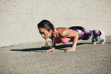 Healthy and muscular young woman doing pushups outdoors. Fitness female doing core exercise in morning. - JLPSF26402