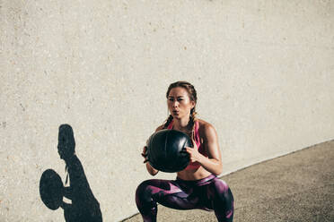 Sportlerin macht Hocke Übungen mit Fitness-Ball. Weibliche Ausübung und Stretching mit Medizinball im Freien. - JLPSF26404