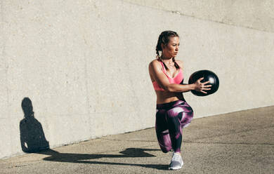 Sportlerin macht Dehnungsübungen mit Medizinball. Muskulöse Frau trainiert mit Fitnessball im Freien. - JLPSF26405