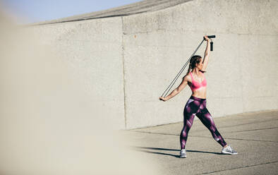 Muskulöse Frau beim Stretching mit Springseil. Weibliches Fitnessmodell beim Stretching-Workout im Freien. - JLPSF26408