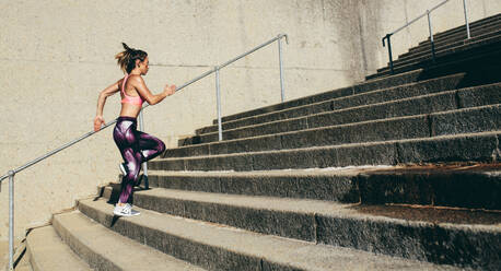 Fitness woman running up on steps. Side view shot of female runner athlete going up stairs. - JLPSF26420