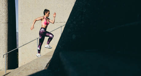 Fit sportswoman climbing up the steps. Female runner exercising on staircase. - JLPSF26421