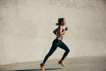 Gesunde junge Frau, die am Morgen läuft. Fitnessmodell, das am Morgen im Freien trainiert. Seitenansicht in voller Länge. - JLPSF26424