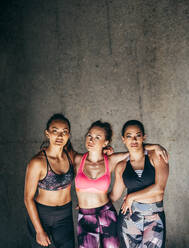 Drei Freundinnen in Sportkleidung stehen nach dem Training zusammen. Porträt von sportlichen jungen Frauen, die in die Kamera schauen. - JLPSF26433