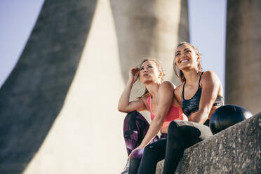 Two fitness females relaxing after workout. Young woman friends sitting outdoors and looking away. - JLPSF26434