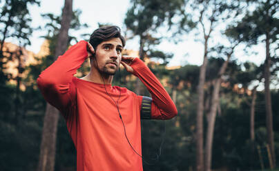 Man wearing earphones looking away. Runner listening to music during morning jog. - JLPSF26441