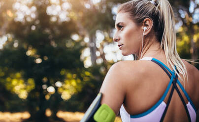 Nahaufnahme einer Sportlerin mit Kopfhörern und einem am Armband befestigten Mobiltelefon. Die Frau hört während des Trainings Musik. - JLPSF26452