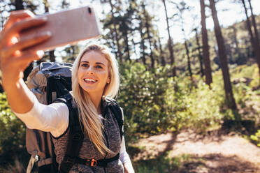 Frau fotografiert mit einem Mobiltelefon beim Trekking. Wanderin macht Selfie beim Trekking im Wald. - JLPSF26469