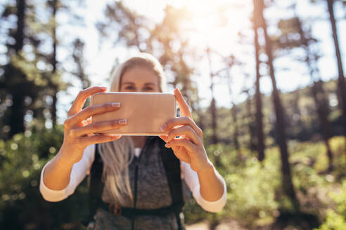 Eine Wanderin schaut auf ihr Handy und hält es mit beiden Händen. Eine Wanderin nutzt ihr Handy zur Navigation im Wald. - JLPSF26472