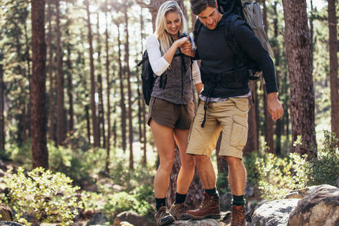 Mann und Frau wandern auf einem felsigen Pfad im Wald. Wandererpaar hält sich an den Händen und geht vorsichtig über Felsen im Wald. - JLPSF26477