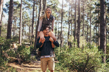 Wanderndes Paar hat Spaß beim Trekking im Wald. Frau reitet huckepack auf Mann beim Wandern im Wald. - JLPSF26479