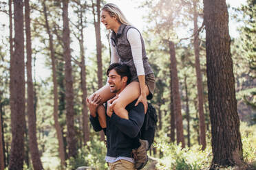 Wanderndes Paar hat Spaß beim Trekking im Wald. Frau reitet huckepack auf Mann beim Wandern im Wald. - JLPSF26482