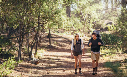 Man and woman hikers trekking on forest trail. Hiker couple exploring nature walking through the woods. - JLPSF26483
