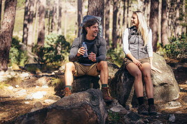 Ein Mann und eine Frau entspannen sich beim Trekking im Wald. Ein Wandererpaar macht eine Pause, sitzt auf einem Felsen und trinkt Wasser. - JLPSF26485