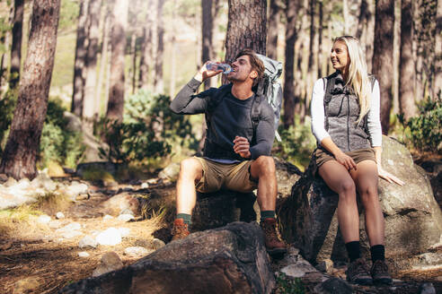 Ein Mann und eine Frau entspannen sich beim Trekking im Wald. Ein Wandererpaar macht eine Pause, sitzt auf einem Felsen und trinkt Wasser. - JLPSF26486