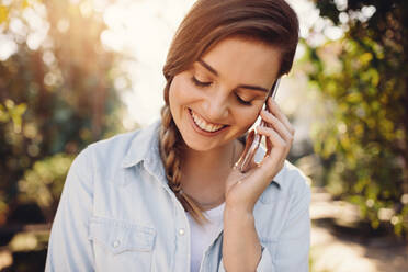 Junge Frau mit Mobiltelefon im Garten. Frau spricht mit Handy und lächelt im Freien. - JLPSF26541