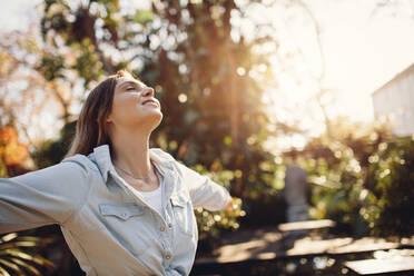 Young female model standing outside with her arms wide open. Woman at park enjoying fresh air. - JLPSF26545