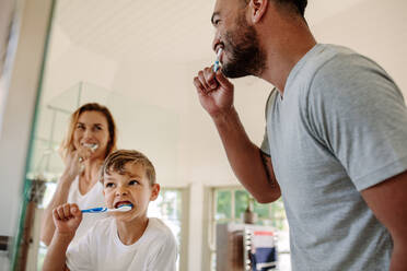 Cute little boy brushing teeth with his father and mother in bathroom. Young family brushing teeth together in bathroom. - JLPSF26550