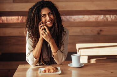 Frau sitzt in einem Restaurant und spricht mit dem Handy. Lächelnde Frau in einem Café mit Kaffee und Snacks auf dem Tisch. - JLPSF26554