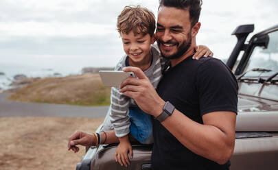 Father with little boy using smart phone together during road trip. Young boy with his father sitting at the front of the car. - JLPSF26572