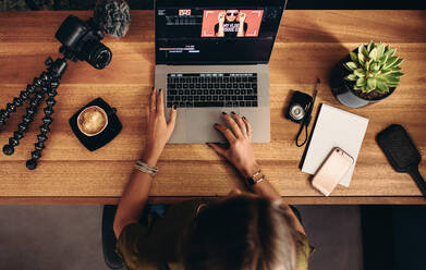 High angle view of female vlogger editing video on laptop. Young woman working on computer with cameras and accessories on table. - JLPSF26584