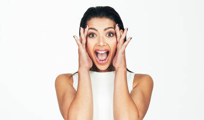 Close up shot of a woman showing an expression of surprise and happiness. Woman holding the sides of her face with her hands and her mouth open in joy. - JLPSF26629